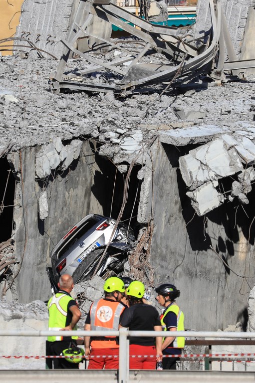Rescuers and police stand near a vehicle caught in the debris of the collapsed Morandi motorway bridge. Photo: Valery Hache / AFP
